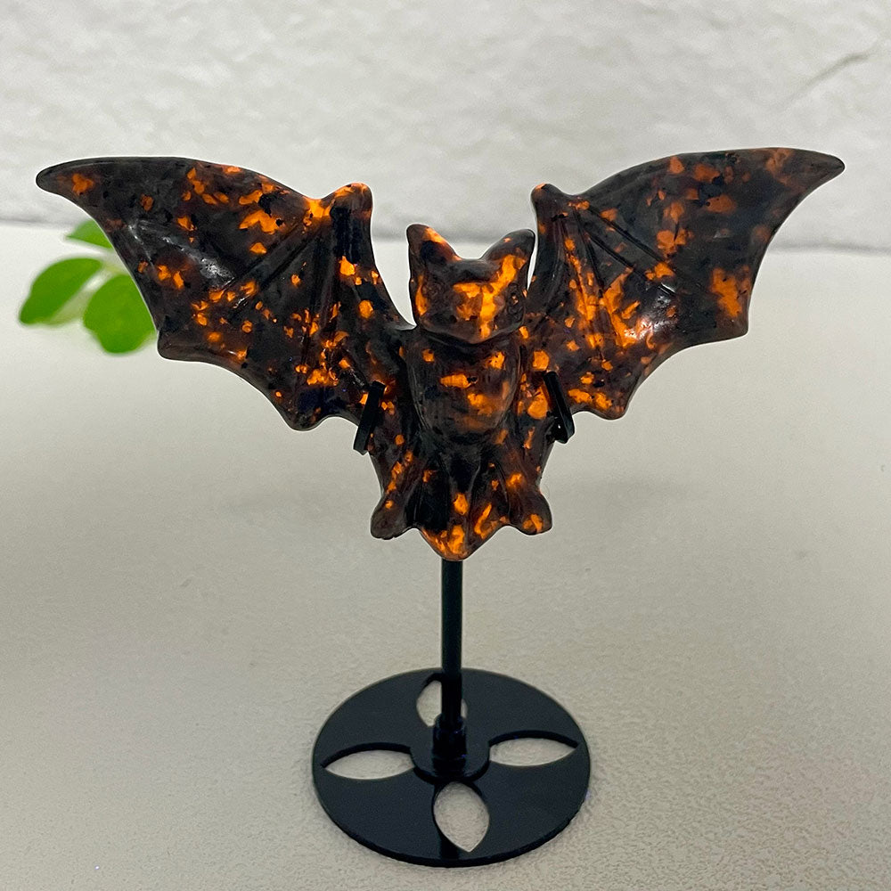 A hand-carved yooperlite crystal bat figurine glowing with vibrant, fiery orange fluorescent spots under a UV blacklight.