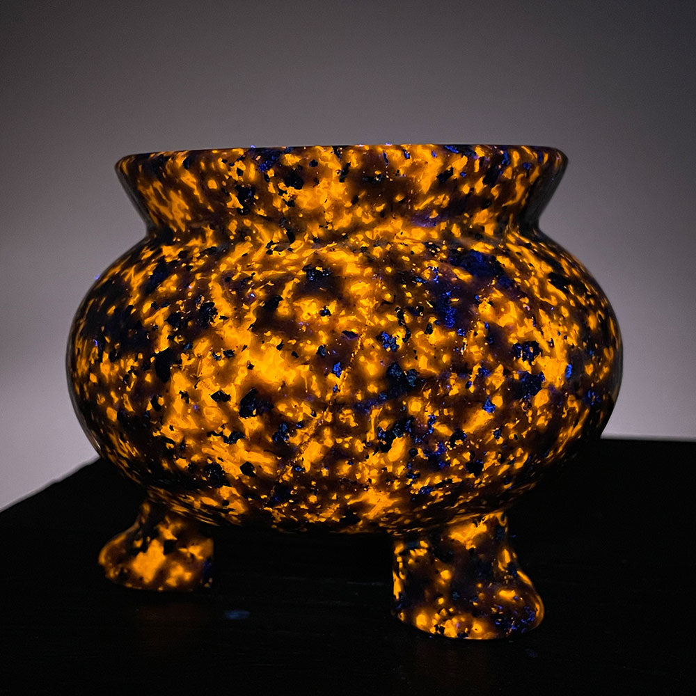 A large stone cauldron glowing bright orange and purple under UV blacklight, resembling magical fire in a dark room.