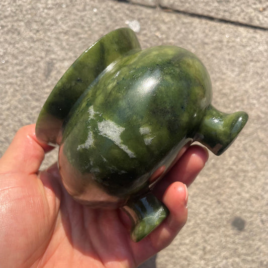 A heavy green serpentine stone cauldron with three legs standing on a table, side view.