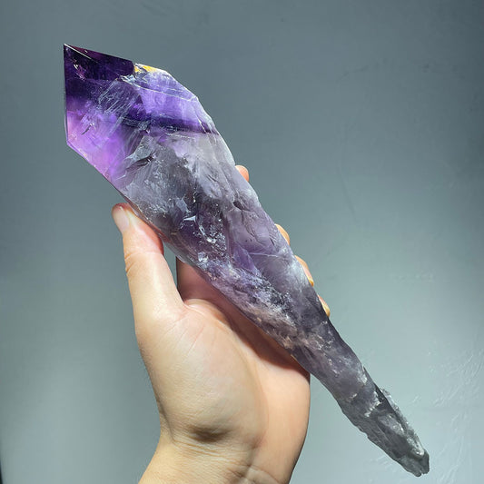 Hand holding a large, raw amethyst scepter wand to show its impressive size.