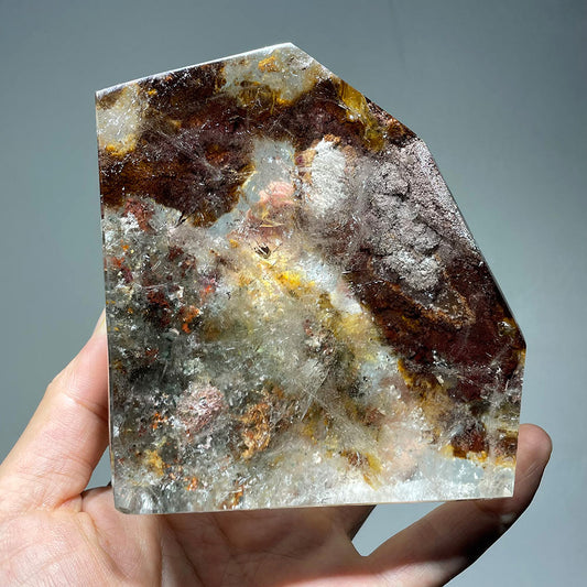 Hand holding a large polished garden quartz freeform with rich red and brown mineral inclusions.