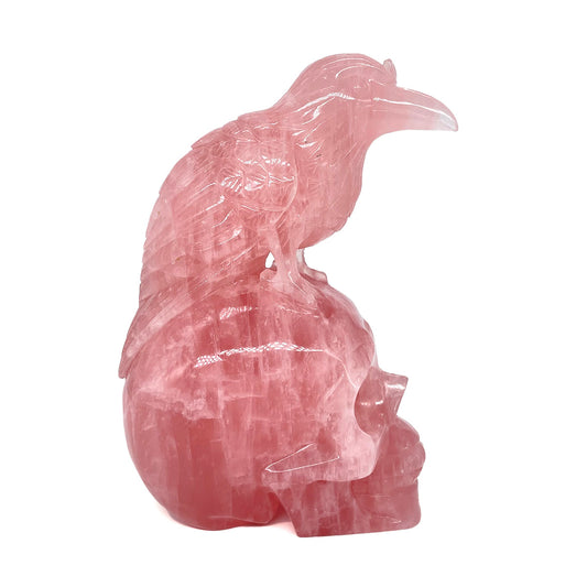 Side view of a large rose quartz carving of a raven perched on a human skull.