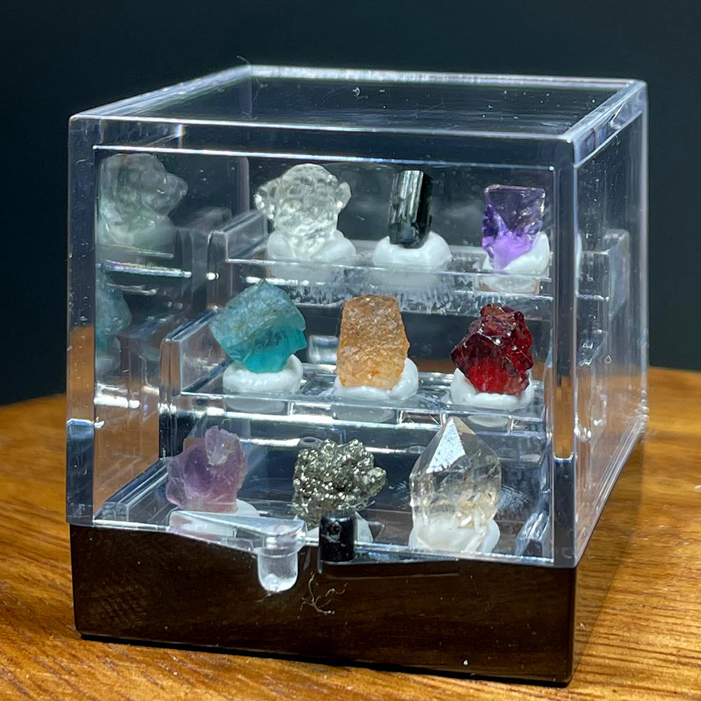 Closeup of a miniature acrylic display box with 9 unique raw crystal specimens on tiered shelves