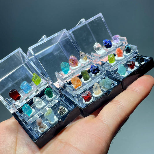 Hand holding several miniature mineral collection boxes showing assorted raw crystals