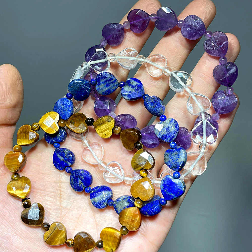 Hand displaying faceted heart bracelets in Amethyst, Lapis Lazuli, Tiger's Eye, and Clear Quartz