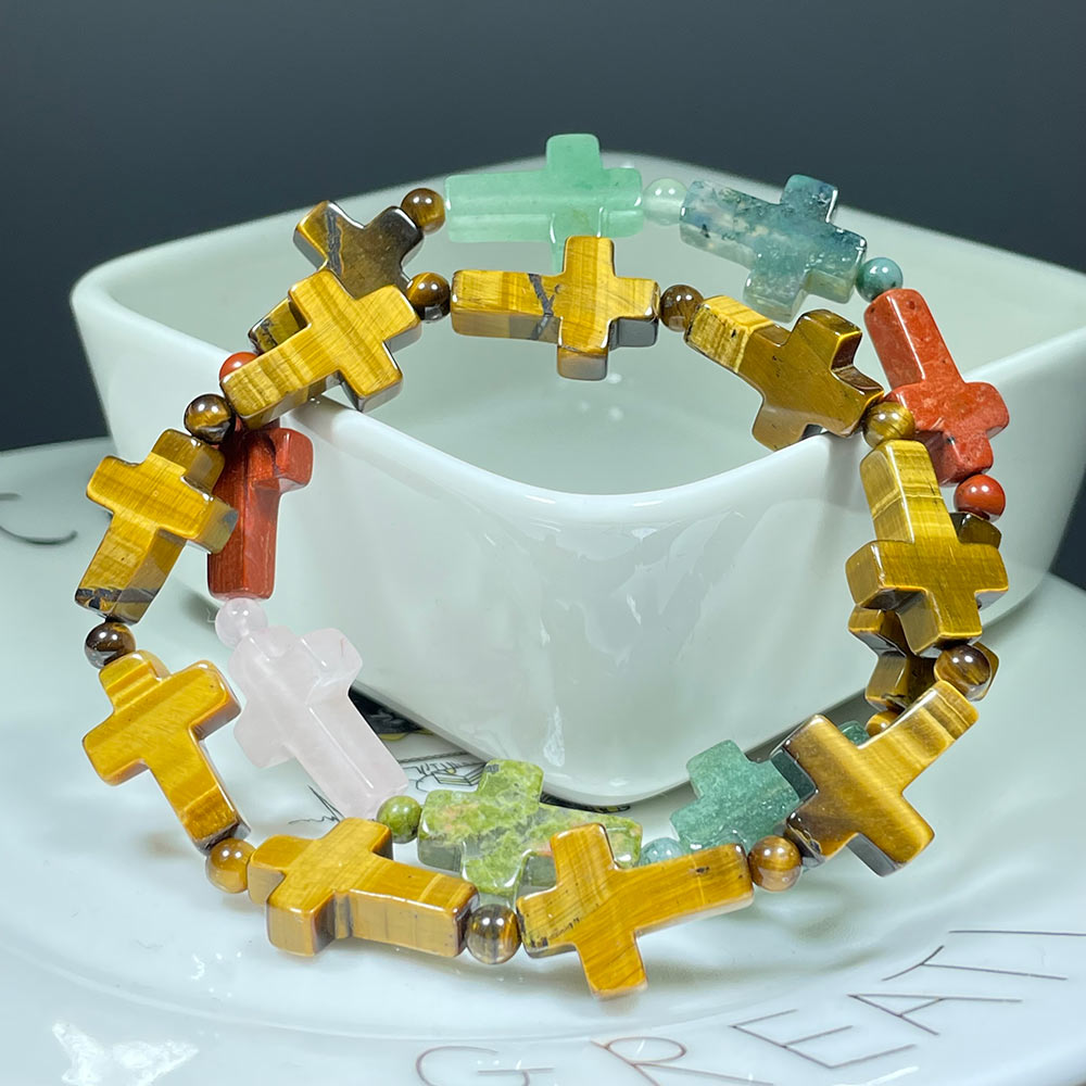 A colorful mixed gemstone cross bracelet displayed on a white dish