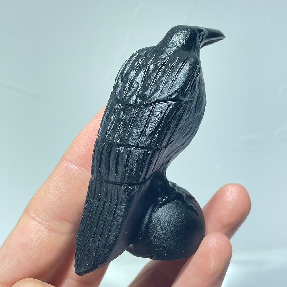 Back view of a black obsidian raven carving showing feather details in hand.