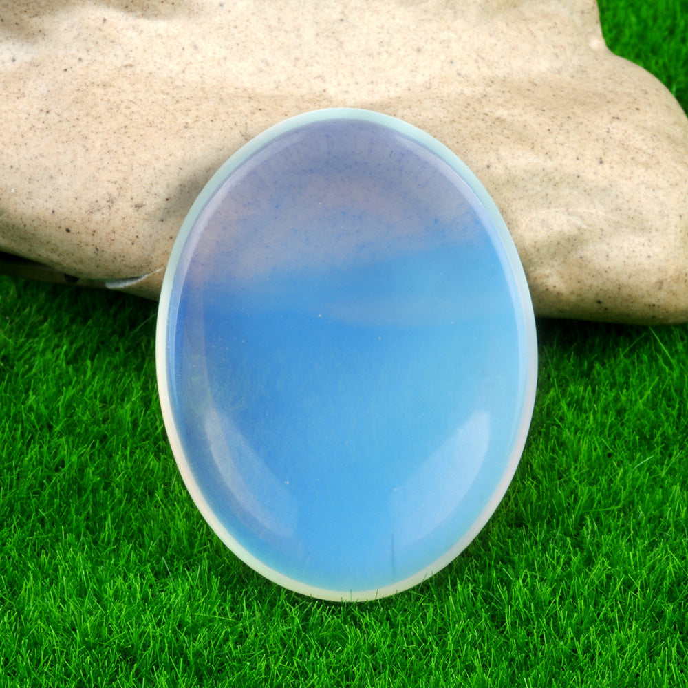 A luminous blue Opalite thumb stone with an ethereal glow, resting on green grass
