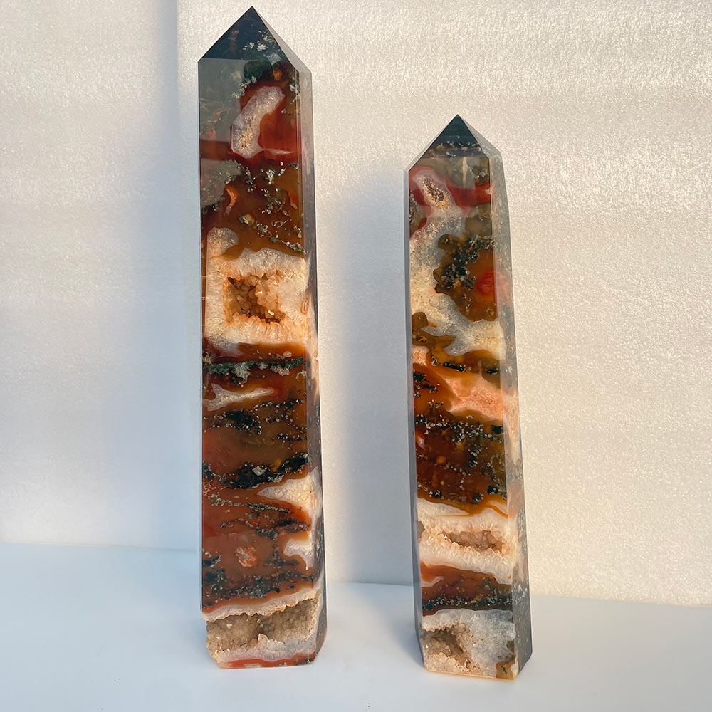 Two large red moss agate crystal towers standing side by side showing red plume patterns and druzy pockets.