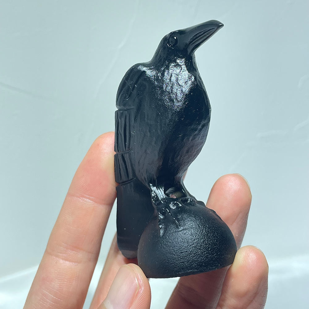 Angled front view of a polished black obsidian raven figurine held in a hand.