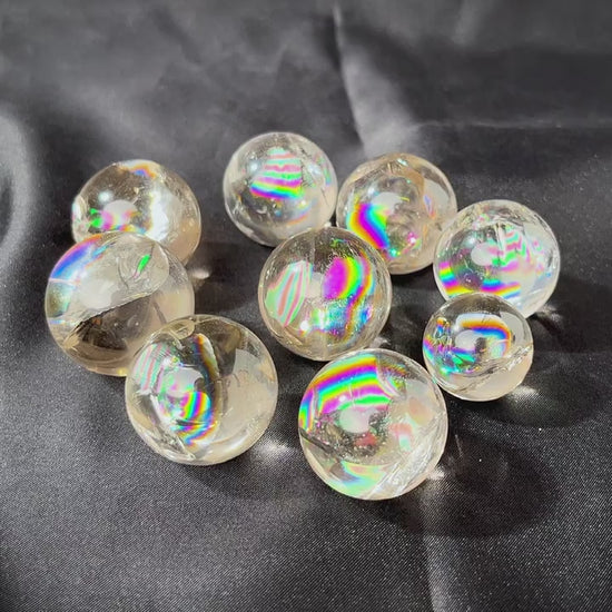 A collection of six mini clear quartz crystal balls with rainbow inclusions on a black surface.