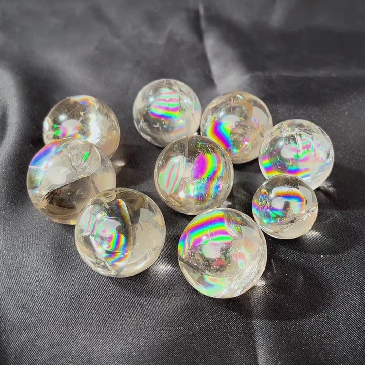 A collection of six mini clear quartz crystal balls with rainbow inclusions on a black surface.