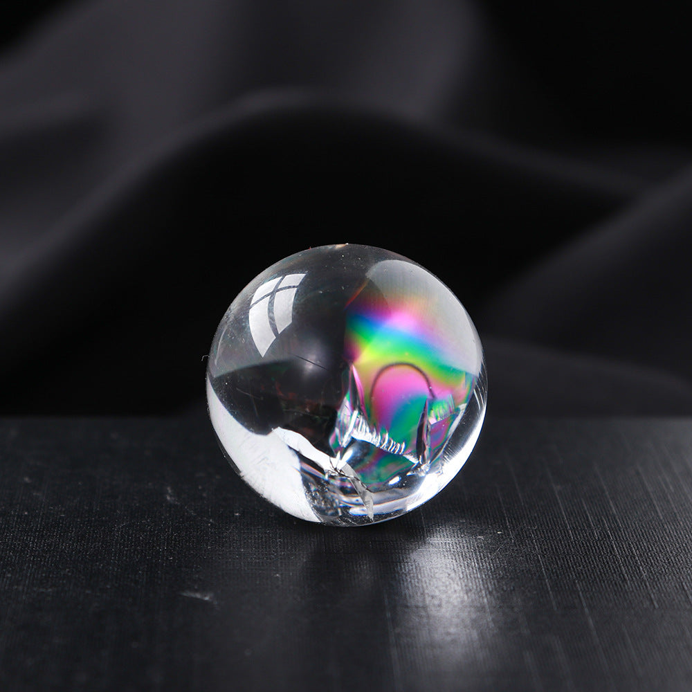 A close-up of a single mini clear quartz sphere with a prominent, colorful rainbow flash