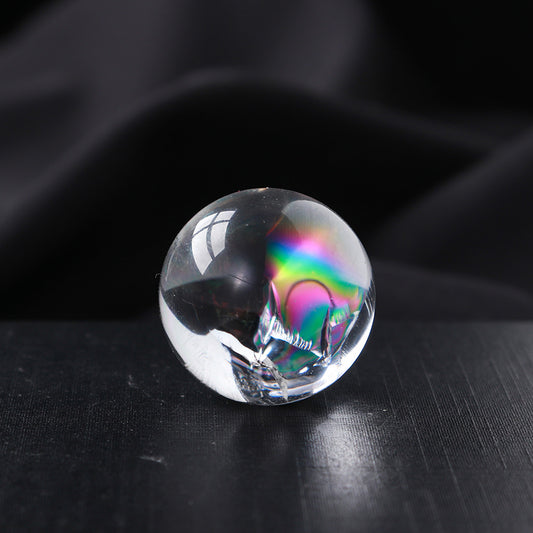 A close-up of a single mini clear quartz sphere with a prominent, colorful rainbow flash