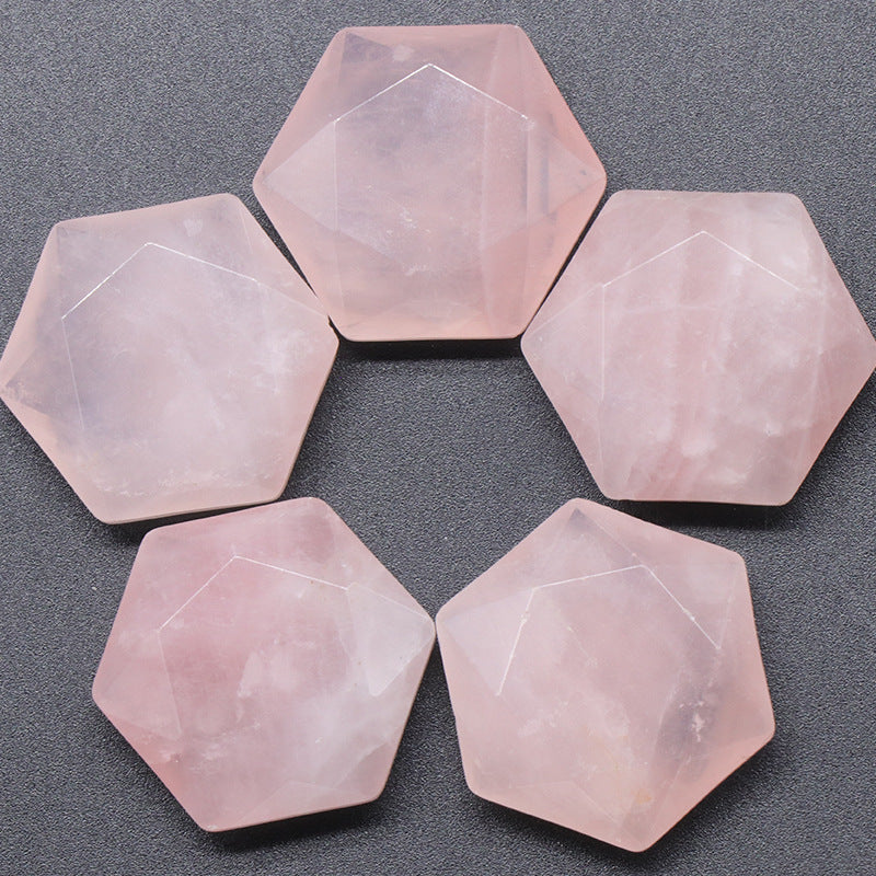 Five light pink rose quartz faceted hexagons arranged on a grey surface.