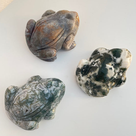Top view of three natural moss agate stone frog carvings with varying green, white, and brown patterns.