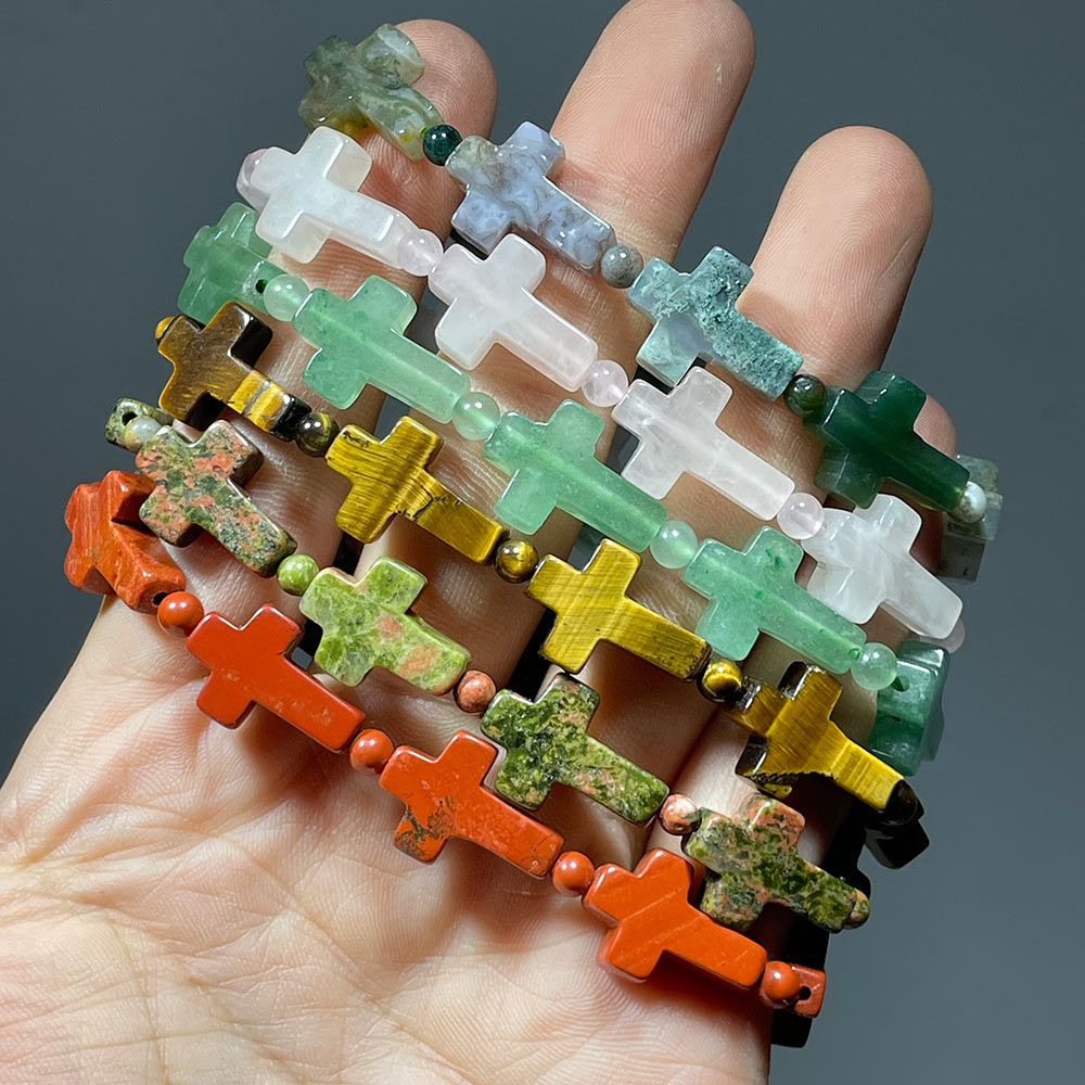A stack of multiple different gemstone cross bracelets worn on fingers to show variety.