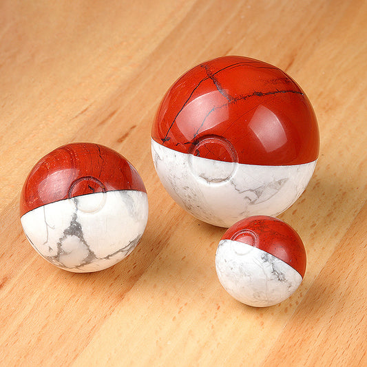 Three red jasper and howlite spheres in small, medium, and large sizes on a wooden table