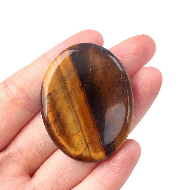Hand holding a polished oval Tiger's Eye worry stone showing its golden chatoyancy